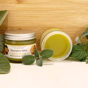 One closed and one open honeybee salve surrounded by herbs